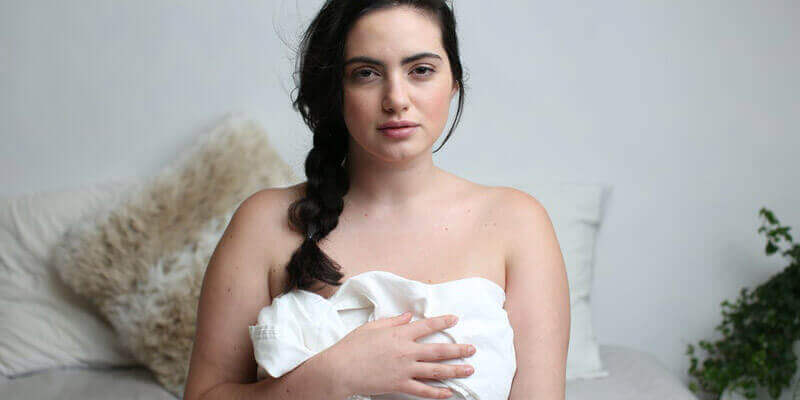 White woman with brunette hair with a white sheet wrapped around her torso